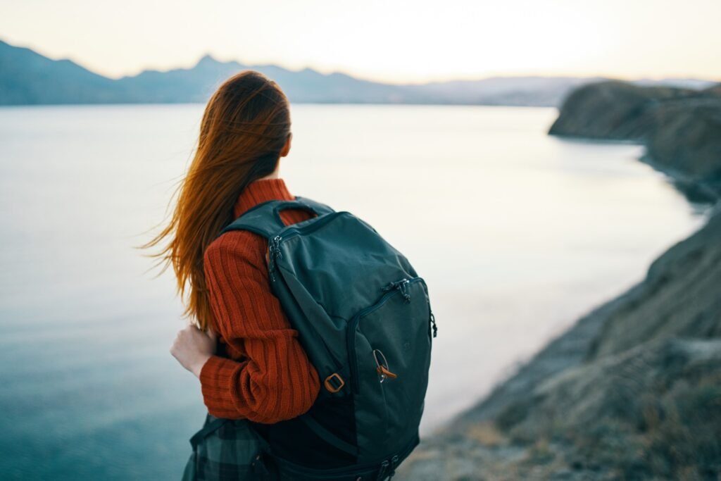 woman in red sweater with backpack and travel tourism sea mountains back view