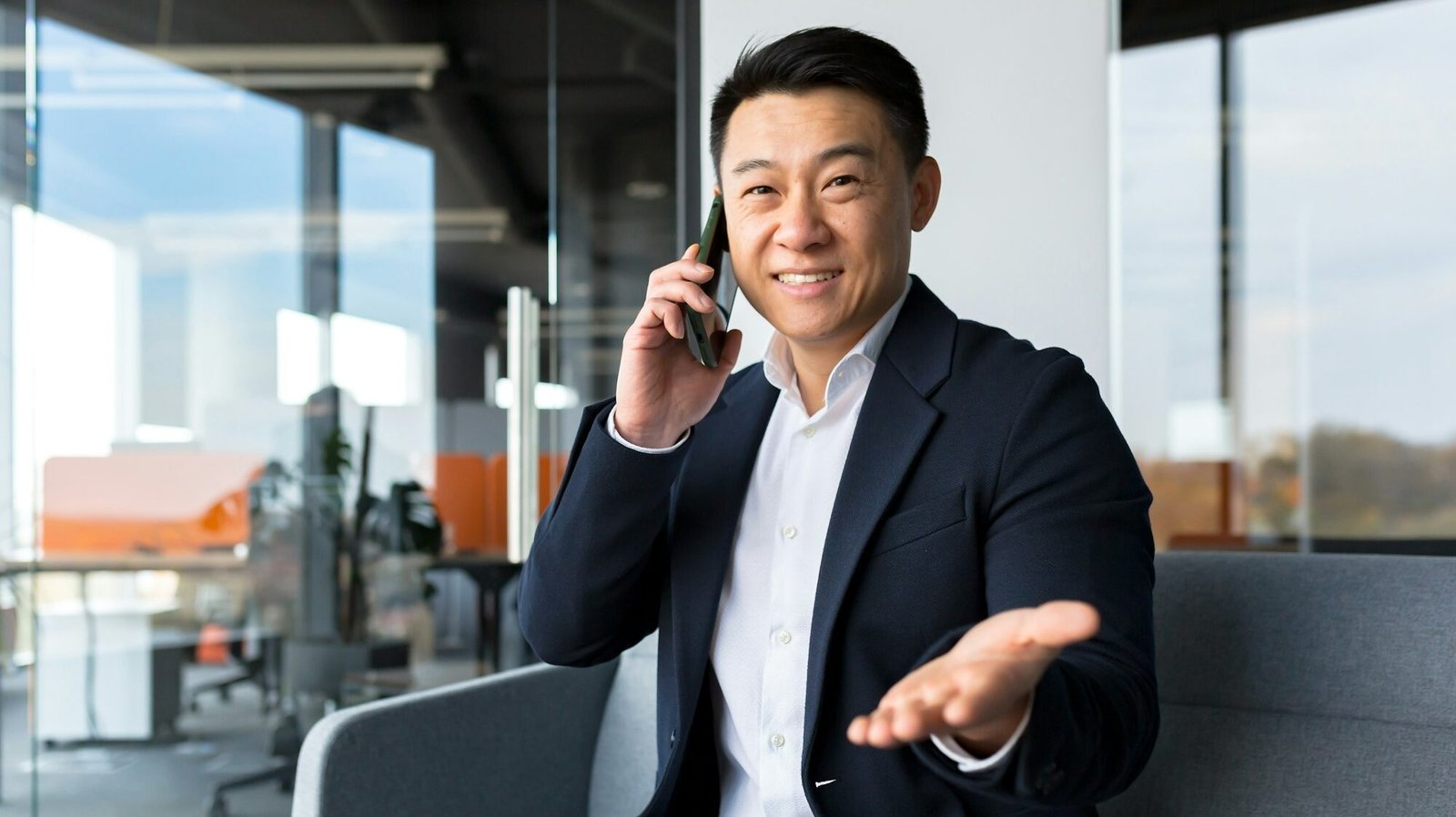 Successful Chinese Asian businessman looks at the camera and smiles talking on the phone